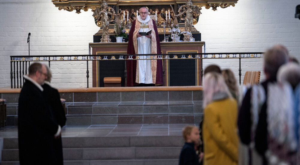 Biskop står foran alter med front mod menighed