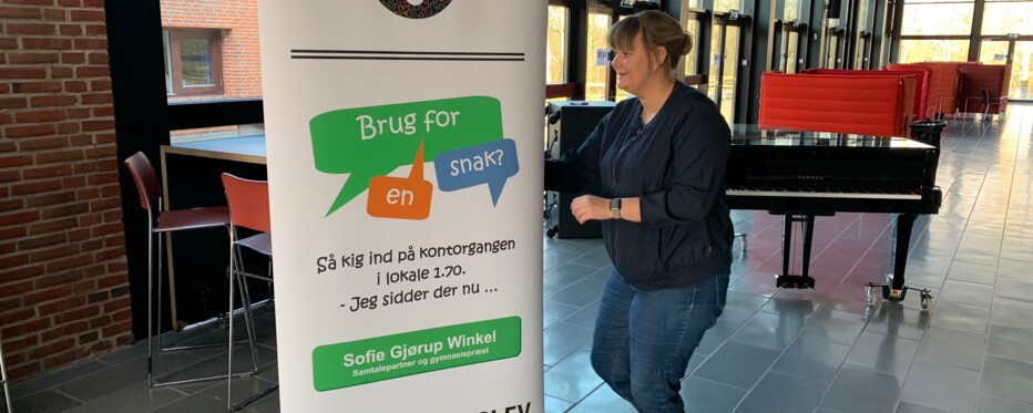 Kvinde står ved skilt med teksten Brug for en snak?